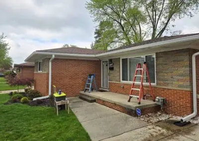 Progress photo of a Michigan brick home during installation of a white aluminum awning with red trim by Wayne Craft
