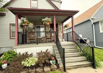 Front view of a residential home with a porch, black railing, and reddish-brown awning built by Wayne Craft